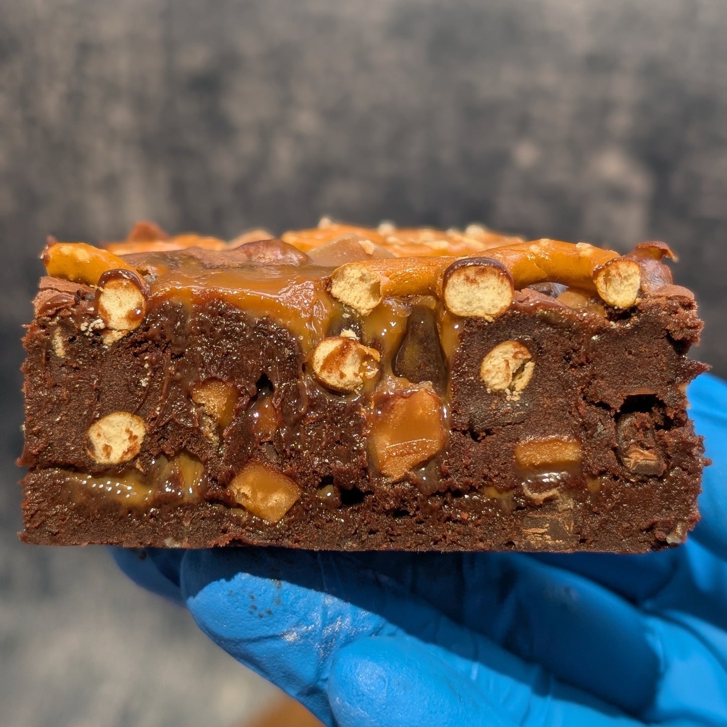 Cross section of brownie showing pretzel pieces, chocolate and fudge chunks and caramel layer.
